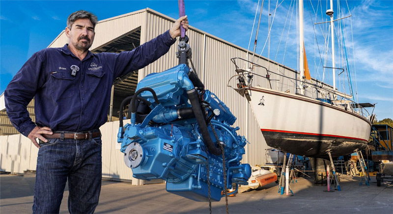 Brian Trautman of SV Delos stands next to a NANNI diesel engine and sailing yacht Delos 1.0 on the hardstand